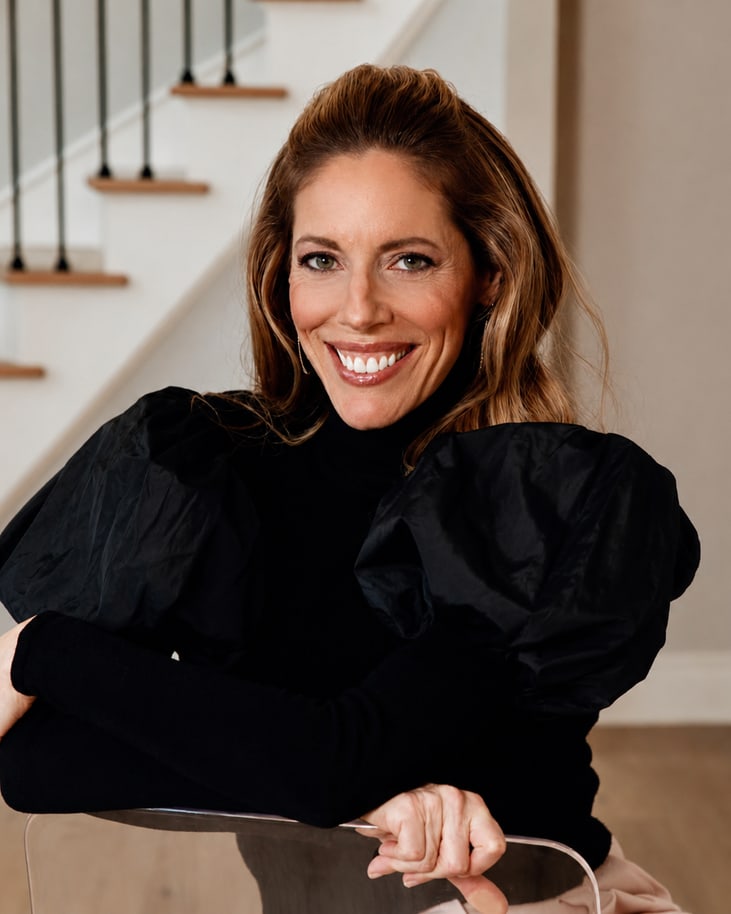 Gilly Stollwerk Garrett smiling warmly in a black puff-sleeve top, leaning on a chair