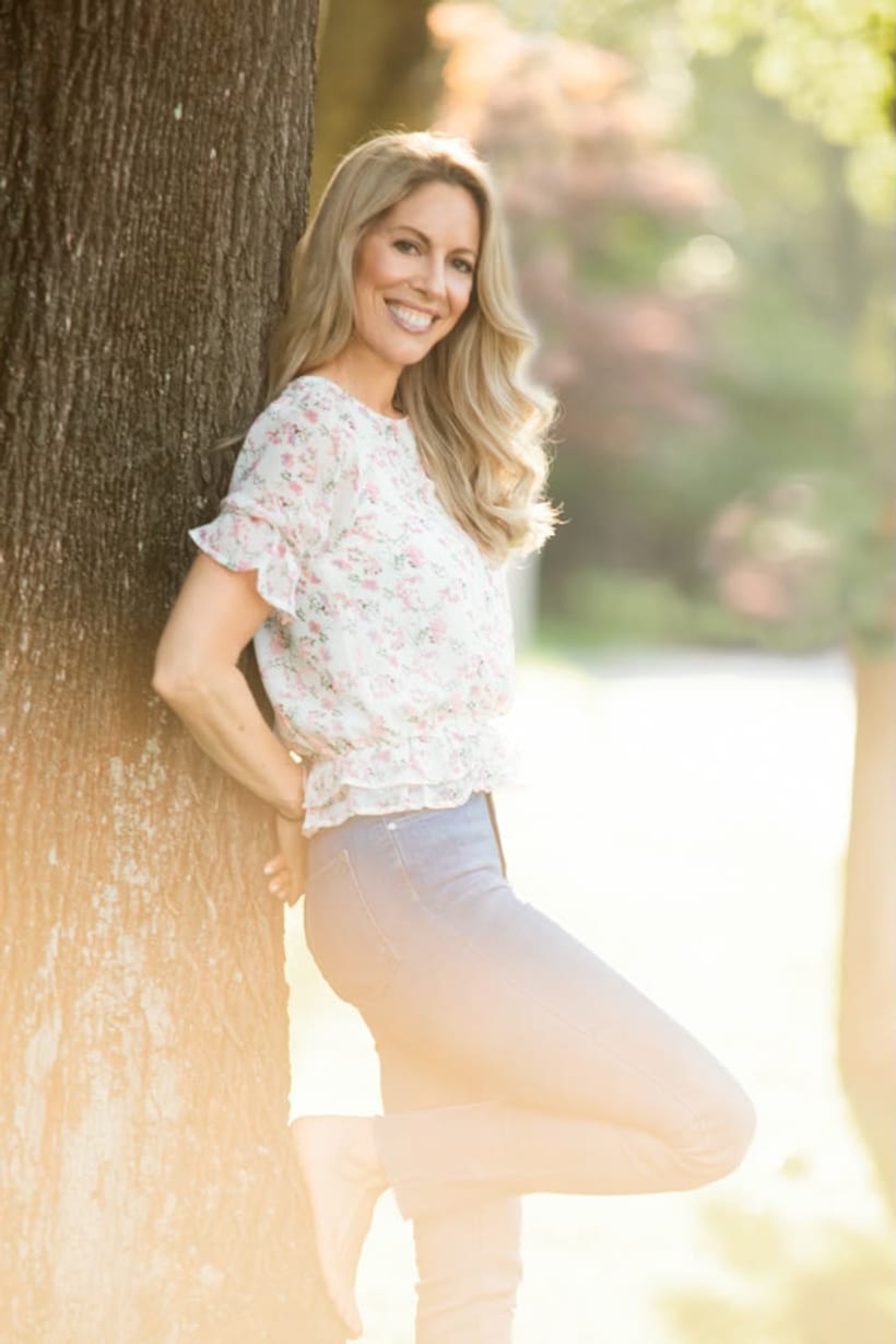 Gilly Stollwerk Garrett smiling outdoors, leaning against a tree in golden light